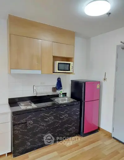 Modern kitchen with sleek black marble countertops and vibrant pink fridge in a compact layout.