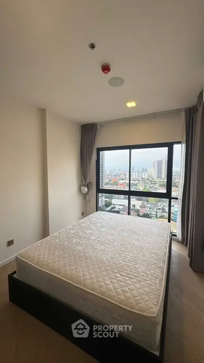 Spacious bedroom with large window offering stunning city views in modern apartment.