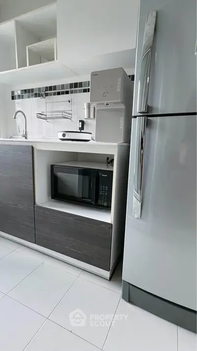 Modern kitchen with sleek appliances and minimalist design, featuring a microwave and fridge.