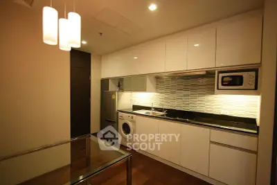 Modern kitchen with sleek cabinets, washing machine, and microwave in a compact layout.