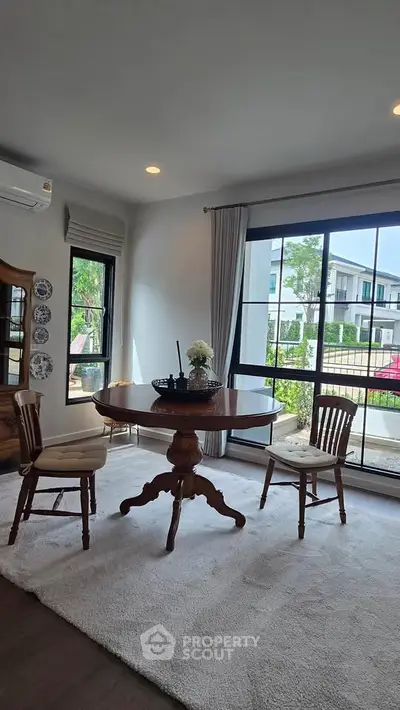 Charming dining area with elegant wooden table, chairs, and large windows offering a serene garden view.