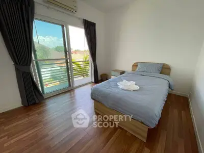 Bright and airy bedroom with hardwood flooring, a comfortable bed, and access to a sunlit balcony with a serene view, perfect for relaxation.