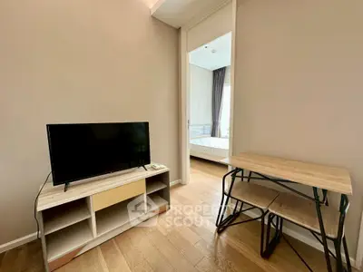 Modern living room with TV and wooden furniture, leading to a cozy bedroom.