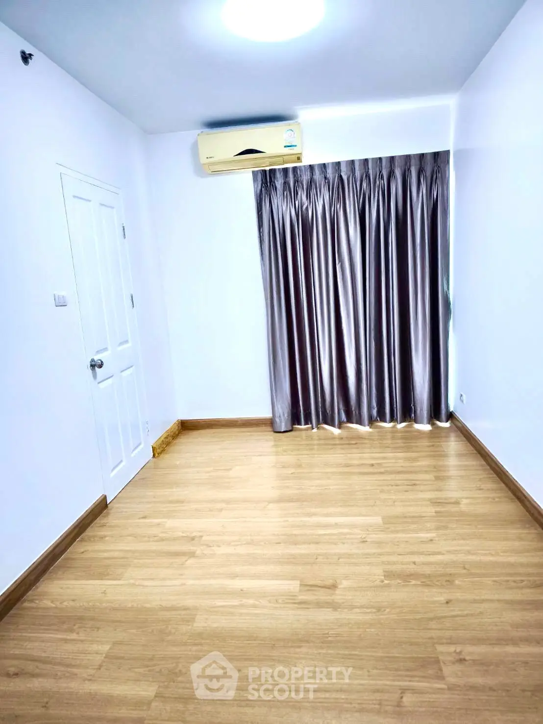 Spacious empty room with wooden flooring and air conditioning, ideal for customization.