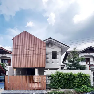 Modern minimalist house exterior with unique facade design and lush greenery.