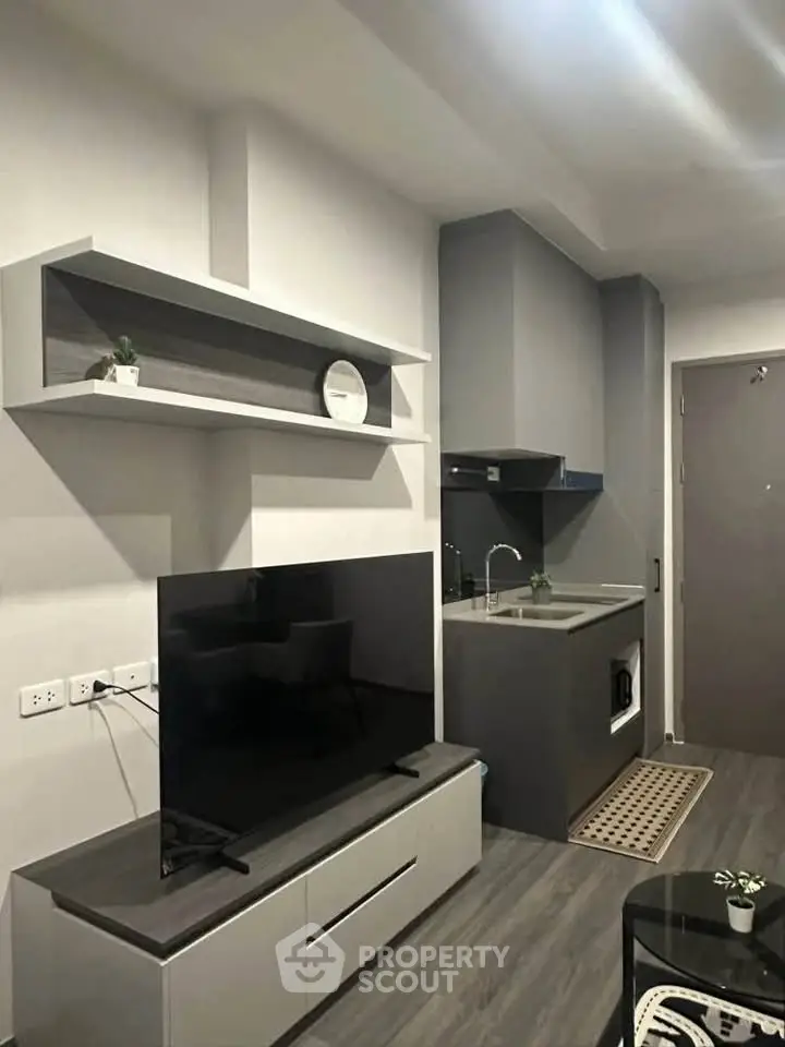Modern living room with sleek TV unit and compact kitchen area in stylish apartment.