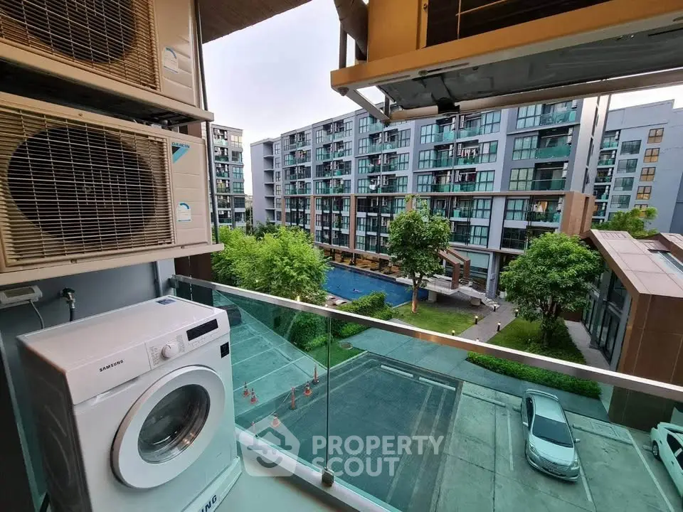 Modern apartment balcony with washing machine and air conditioning units overlooking pool and garden.
