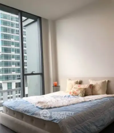 Modern bedroom with large window and city view in high-rise apartment.