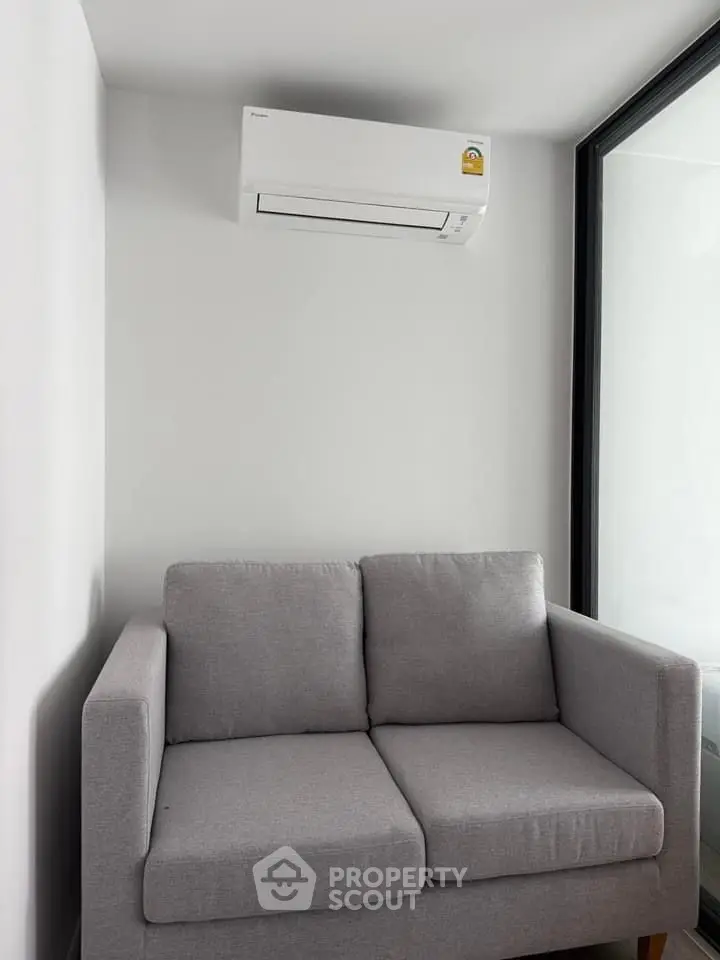 Modern living room with gray sofa and wall-mounted air conditioner in a bright, minimalist space.