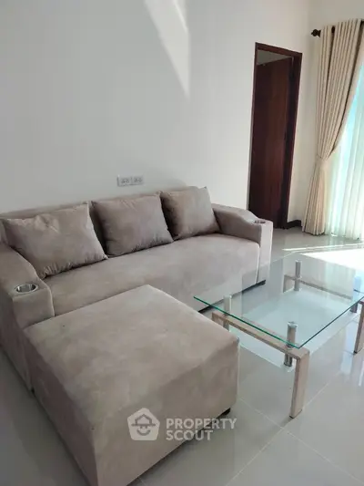 Modern living room with plush sofa and glass coffee table in bright, airy space.