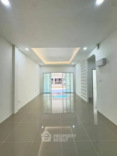 Spacious modern living room with glossy tiled floors and recessed lighting, featuring a glass sliding door leading to a pool view.