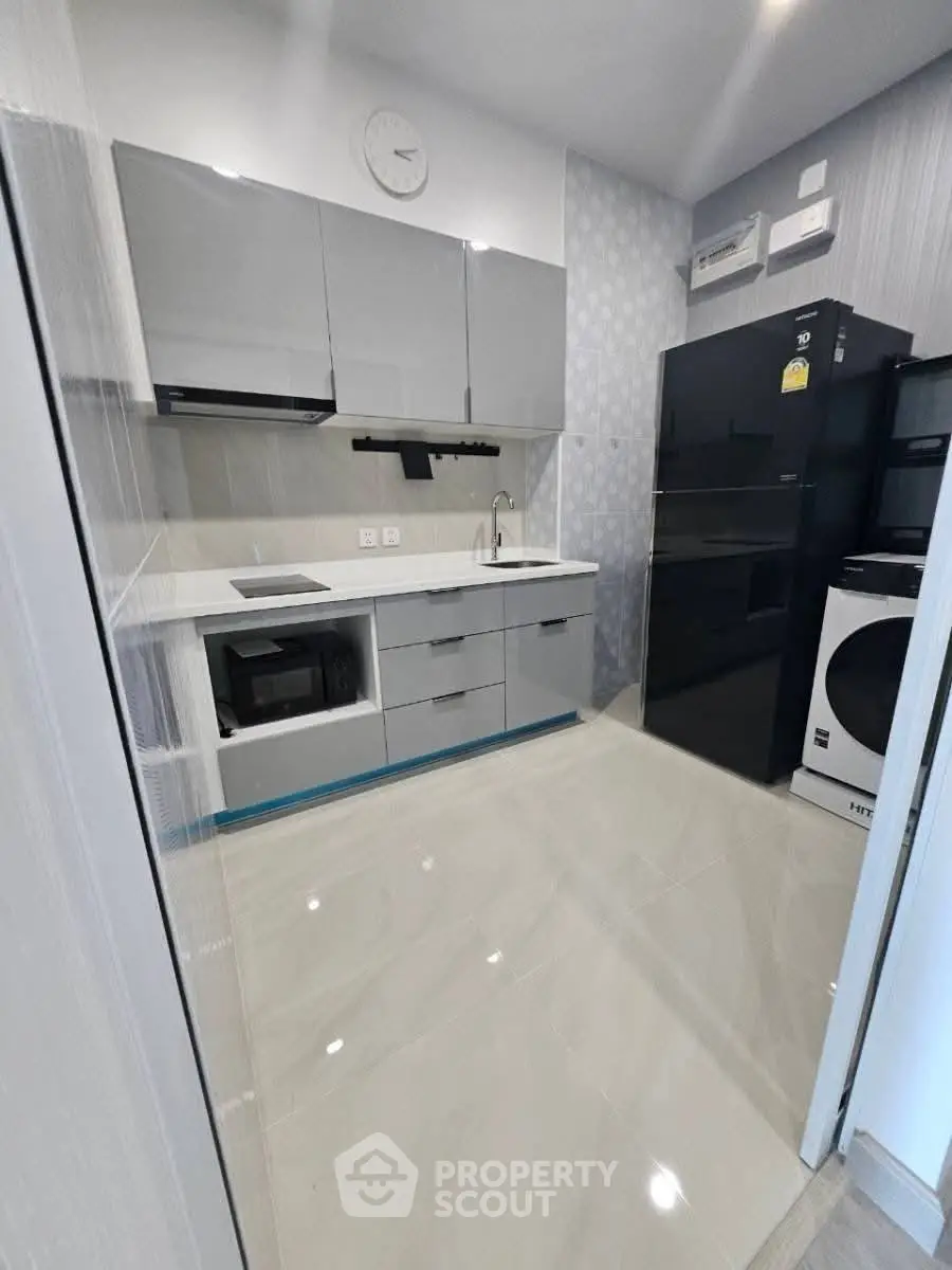 Modern kitchen with sleek cabinetry and appliances, featuring a washing machine and microwave.