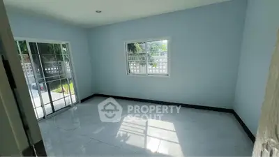 Bright empty room with large windows and sliding glass door opening to garden view.