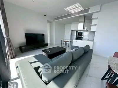 Modern living room with open kitchen, sleek furniture, and abundant natural light.