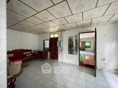 Spacious interior with tiled floors and floral ceiling, featuring wooden furniture and glass door entry.