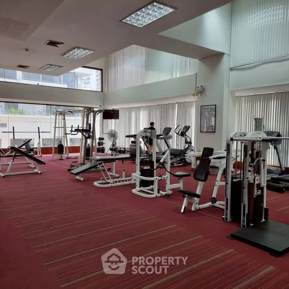Spacious gym with modern fitness equipment and large windows in a residential building.