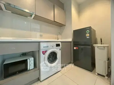 Modern kitchen with washing machine, microwave, and fridge in sleek design.