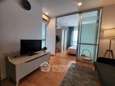 Modern living room with wooden flooring, TV stand, and view into a cozy bedroom with natural light.