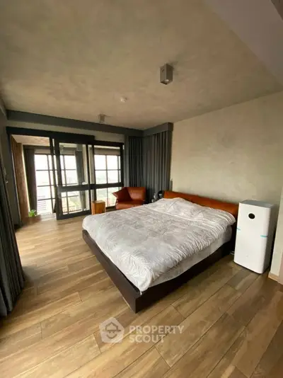 Spacious modern bedroom with wooden flooring and large windows offering natural light.