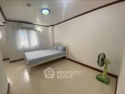 Spacious bedroom with minimalist decor and natural light, featuring a comfortable bed and a standing fan.