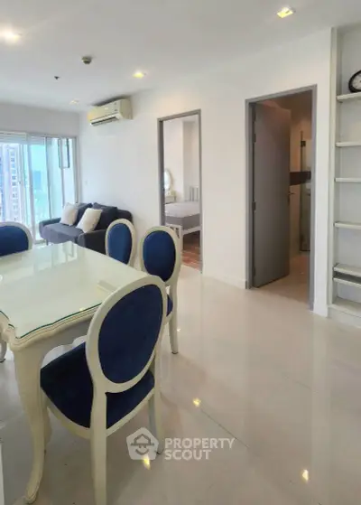 Modern apartment interior with dining area and view into bedroom, featuring elegant blue chairs and sleek design.