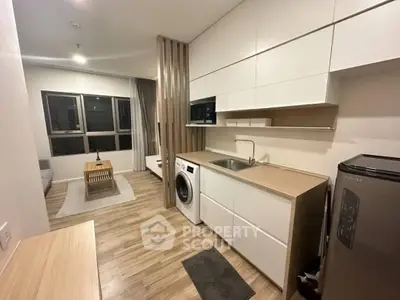 Modern open-layout kitchen with washing machine and cozy living area in stylish apartment.