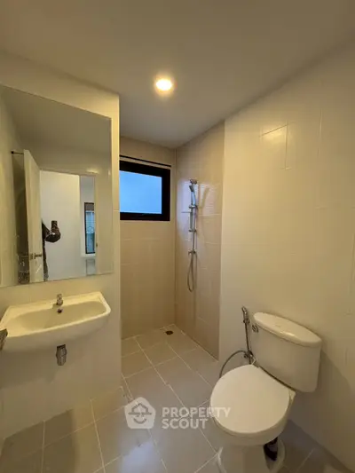 Modern bathroom with sleek fixtures and neutral tiles, featuring a shower and toilet.
