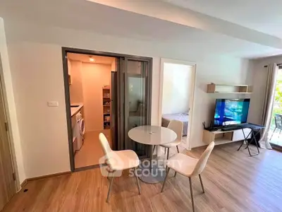 Modern living room with open layout, featuring a cozy dining area and a view into a bedroom and laundry space.