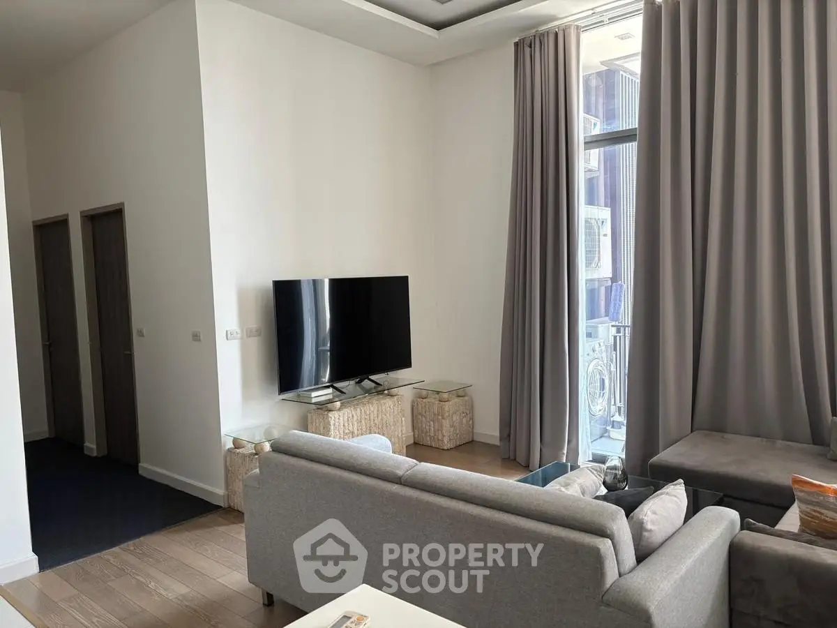 Modern living room with sleek furniture and large TV, featuring floor-to-ceiling windows and elegant curtains.