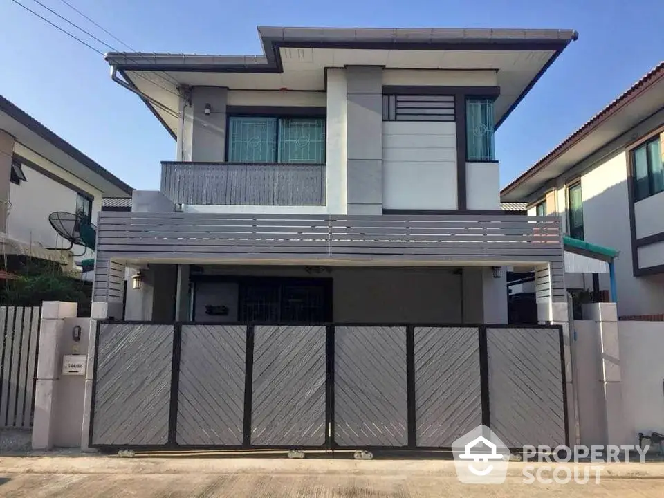 Modern two-story house with gated entrance and sleek design in suburban neighborhood.