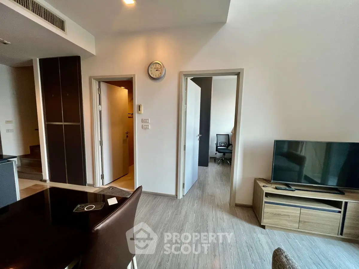 Modern living space with dining area, TV, and office room, featuring sleek wooden flooring.