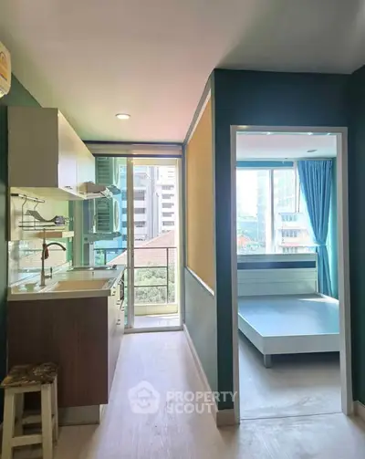 Modern apartment interior with kitchen and bedroom, featuring large windows and city view.