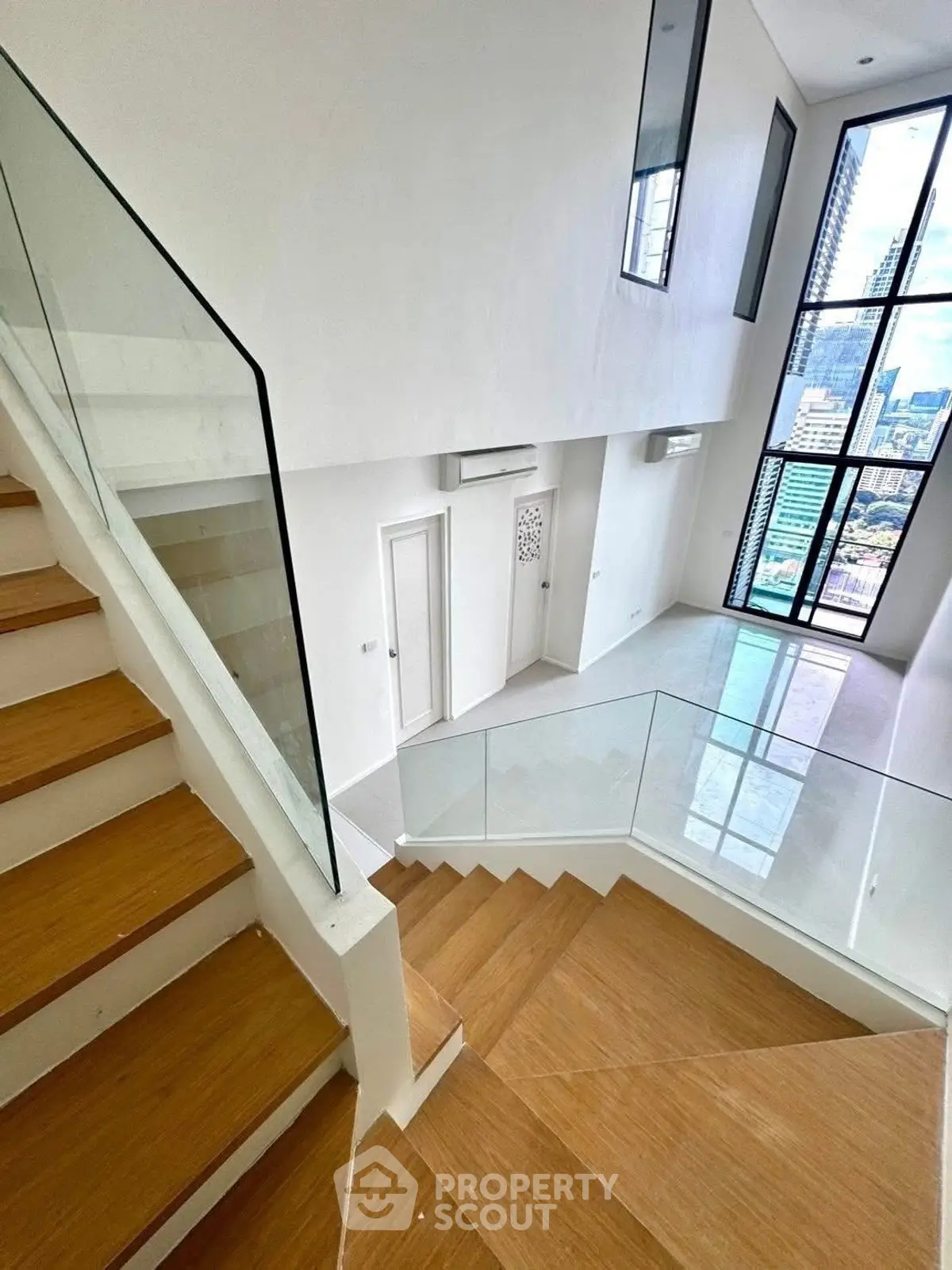 Modern duplex interior with wooden staircase and large windows offering city views.
