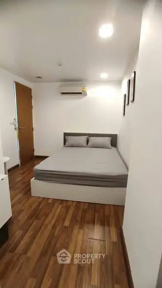 Cozy bedroom with modern decor and wooden flooring, featuring a comfortable bed and air conditioning.