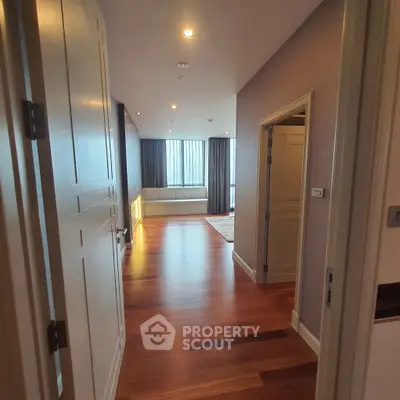 Spacious hallway leading to a bright living area with wooden flooring and large windows.