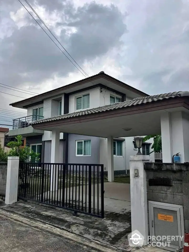 Modern two-story house with gated entrance and driveway under cloudy sky.