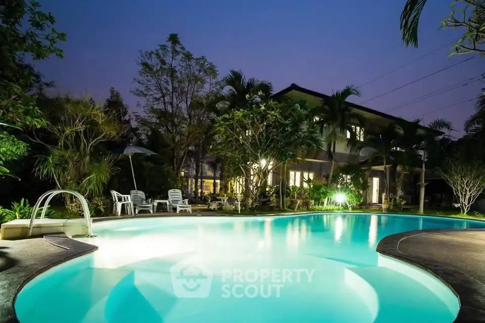 Luxurious villa with illuminated pool and lush garden at dusk, perfect for serene living.