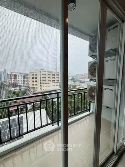 Modern balcony with city view and air conditioning units on a rainy day.