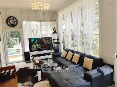 Spacious living room with large windows and pool view, featuring modern black leather sofa and elegant decor.