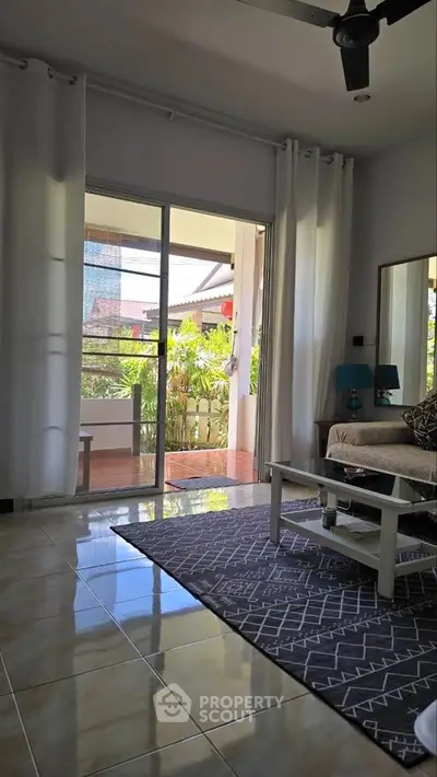 Charming living room with large windows opening to a lush balcony view, featuring cozy seating and elegant decor.