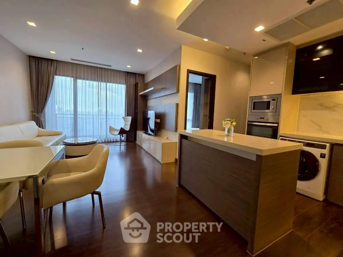 Modern open-plan living room with kitchen, featuring sleek furniture and large windows.