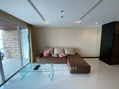 Spacious living room with modern sofa and glass coffee table, featuring large windows and balcony access.
