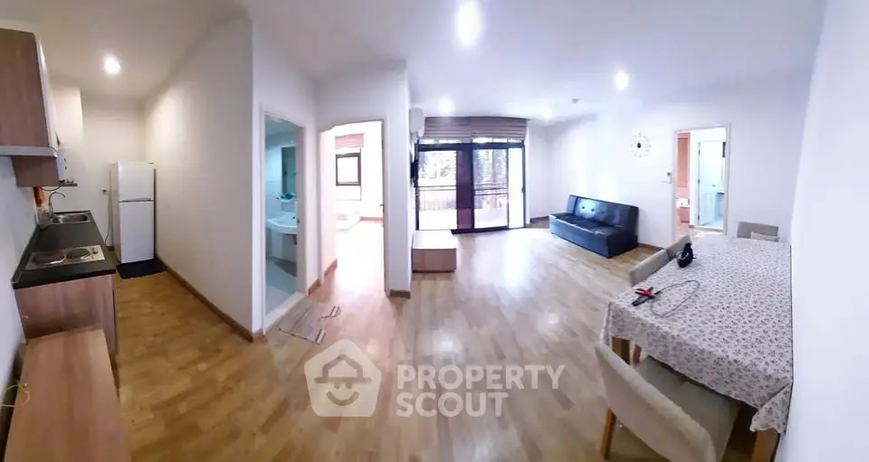 Spacious open-plan living room with kitchen and balcony access, featuring modern furnishings and natural light.