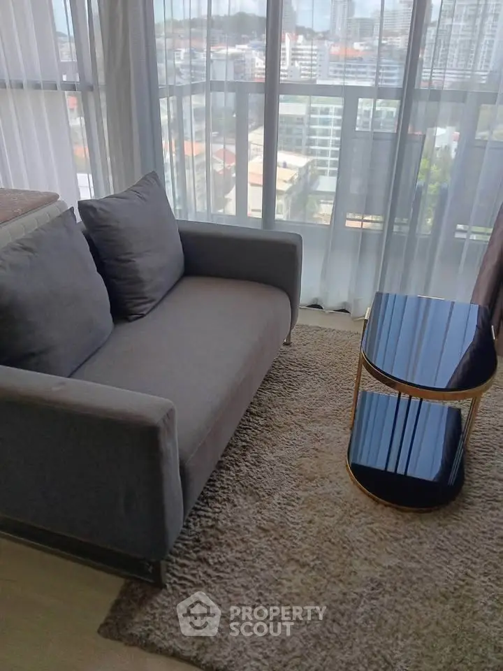 Modern living room with cozy gray sofa and glass table, offering a stunning city view through large windows.