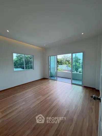 Spacious room with wooden flooring and balcony access, offering a serene view.
