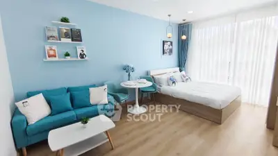 Modern studio apartment with blue accents, featuring a cozy bed and stylish seating area.