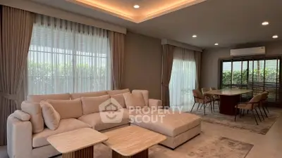 Elegant living room with plush sofa and dining area, featuring large windows and modern lighting.