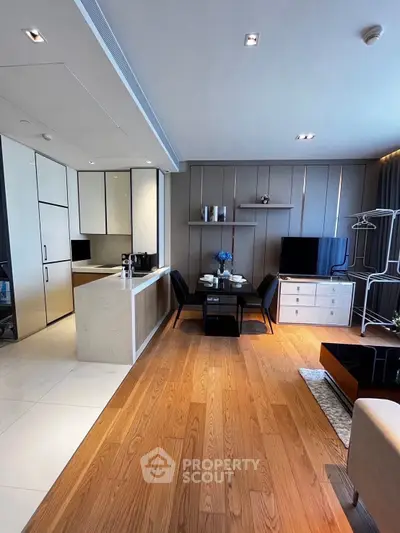Modern open-layout living room with sleek kitchen and dining area, featuring elegant wood flooring and contemporary decor.