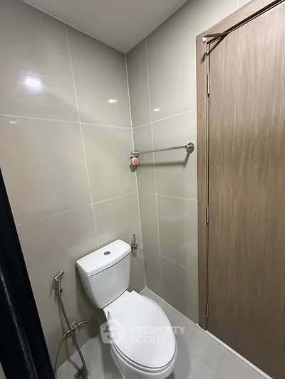 Modern bathroom with sleek design and neutral tiles, featuring a toilet and towel rack.