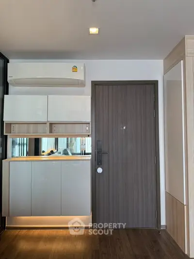 Modern apartment entrance with sleek cabinetry and air conditioning unit.